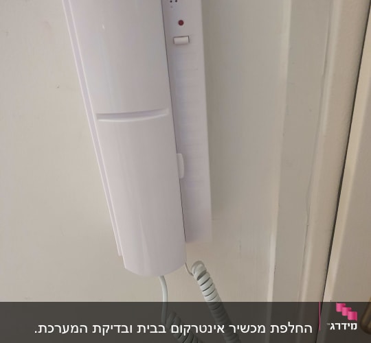 אינטרקום לבן מותקן על קיר עם חוט מסולסל